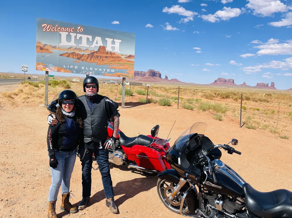 Annie and Al with their motorcycles beside the Welcome to Utah sign on a US riding trip